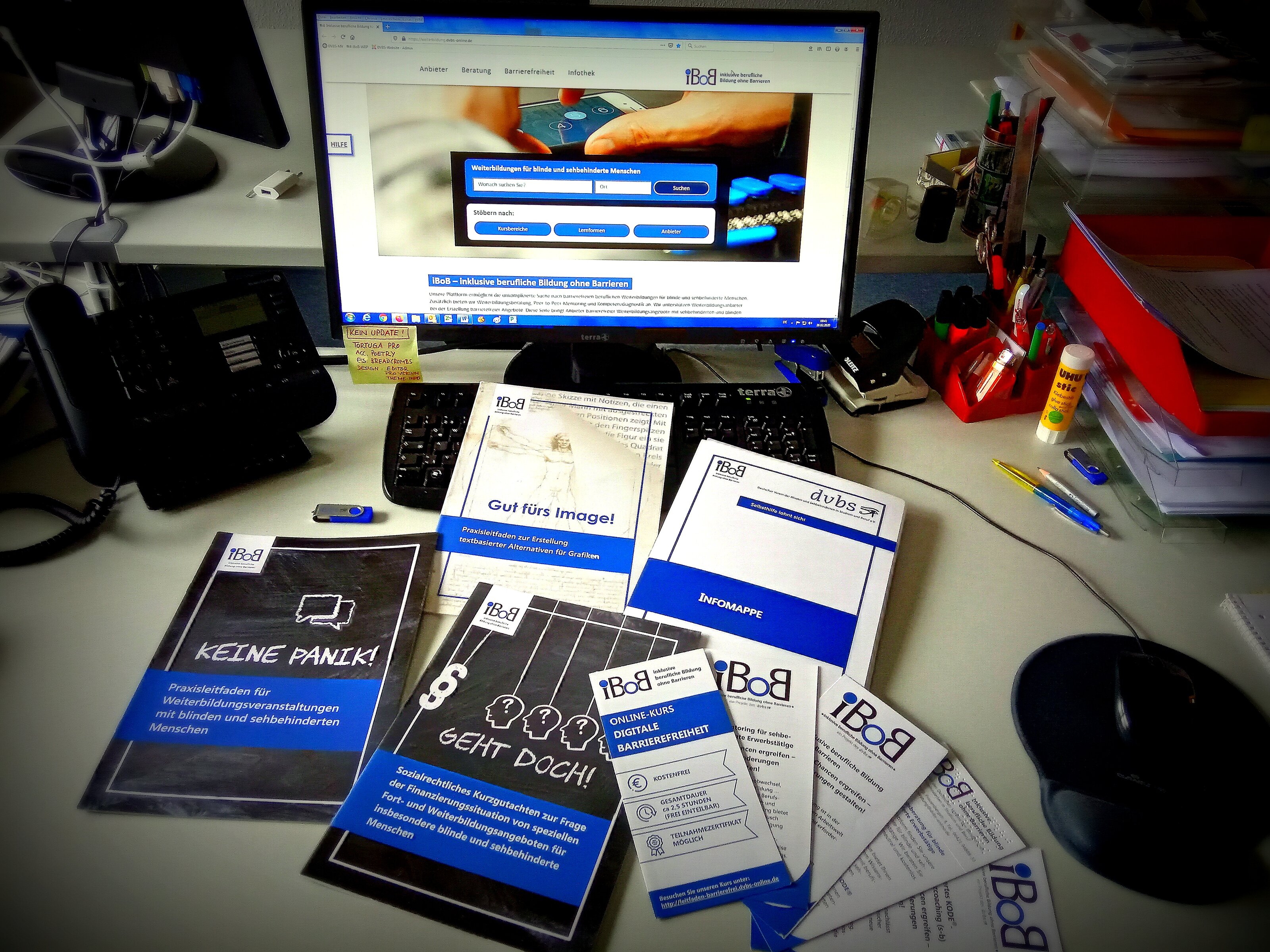 Foto: Schreibtisch mit iBoB-Broschüren und PC-Monitor, der die iBoB-Weiterbildungsplattform zeigt